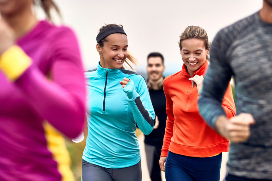 Happy athletic women having fun while jogging with group of people in nature.